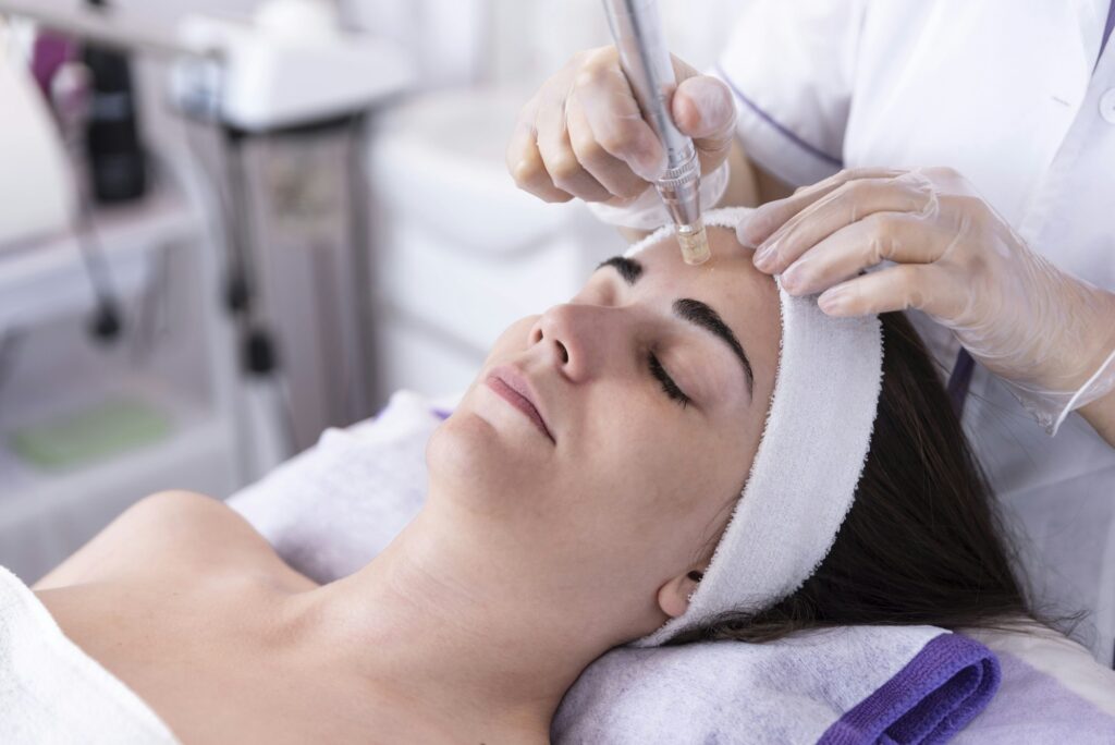 beautician applying facial dermapen treatment on face of young woman