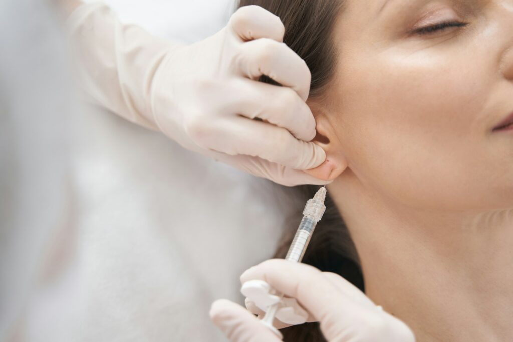 Doctor cosmetologist making beauty injection in woman ear