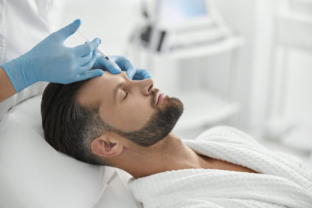 Professional cosmetologist does injection at eyebrow lifting procedure to mature man in clinic